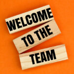 "Welcome to the team" spelled out on wooden blocks on a bright orange background.